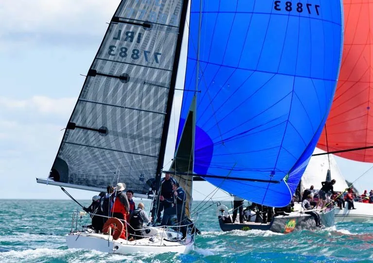 Olson 30 IRL 77883 racing upwind under grey mainsail and jib, crew hiking, as rivals fly blue and red spinnakers