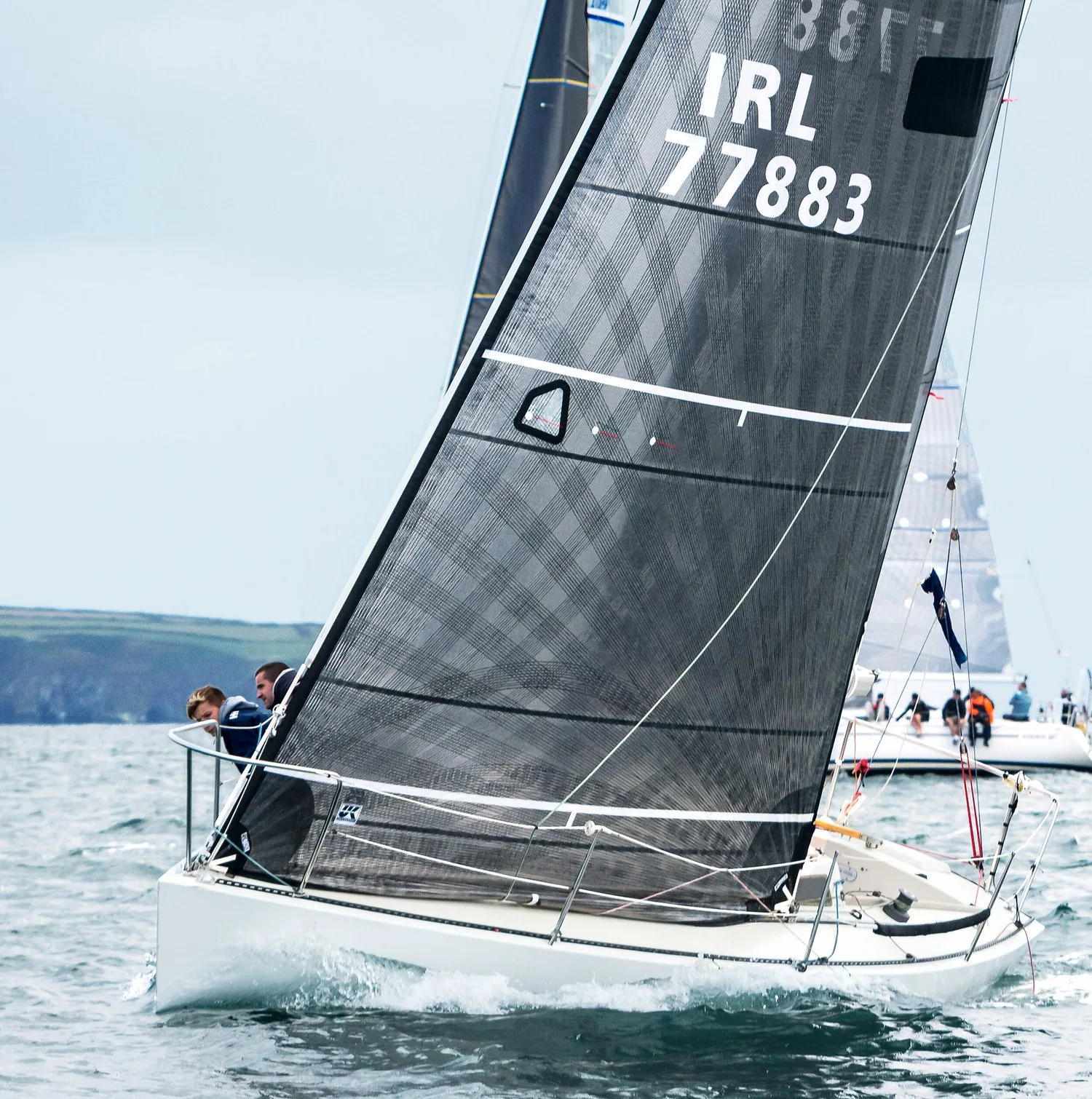 Olson 30, IRL 77883, close-hauled under a grey mainsail and jib off the Irish coast, crew at the bow