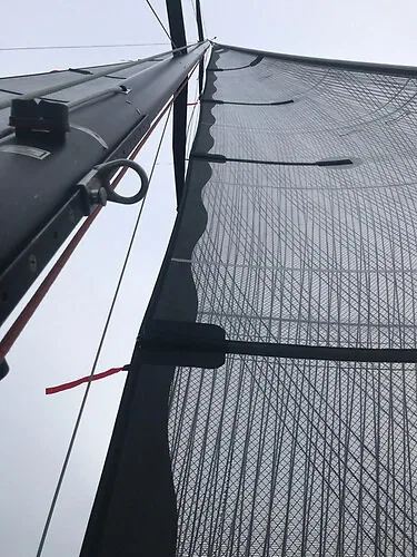 Looking up a black carbon load-path mainsail from the boom, full battens and mast at left
