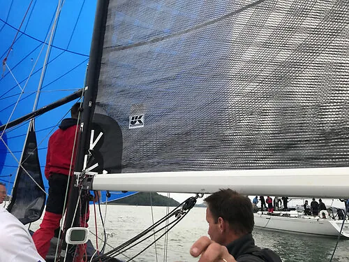 Grey carbon mainsail with UK Sailmakers logo seen from the cockpit, blue spinnaker set and crew forward