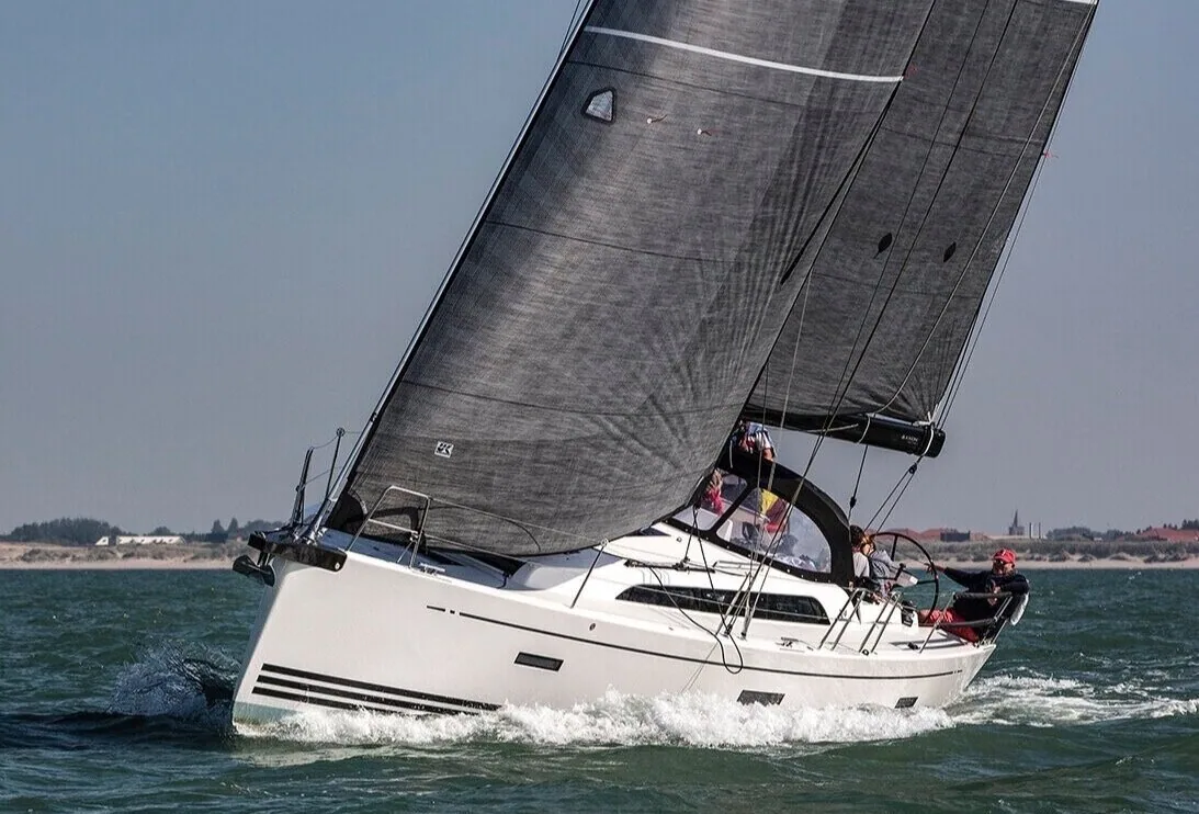 X4.0 sailing upwind under grey X-Drive® LiteSkin mainsail and genoa, crew in red jackets, low coastline behind