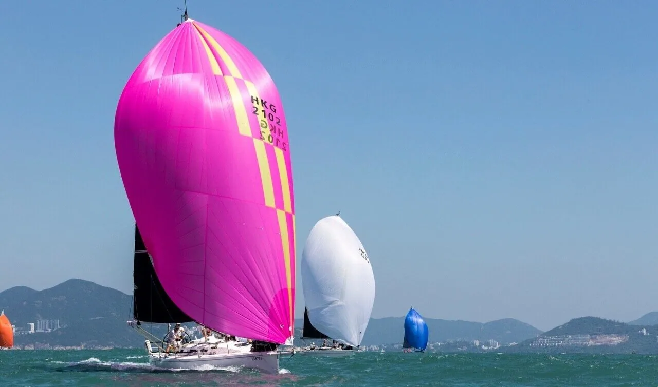 J/109 WHISKEY JACK running under a magenta asymmetric spinnaker with yellow stripes and HKG sail number, others astern