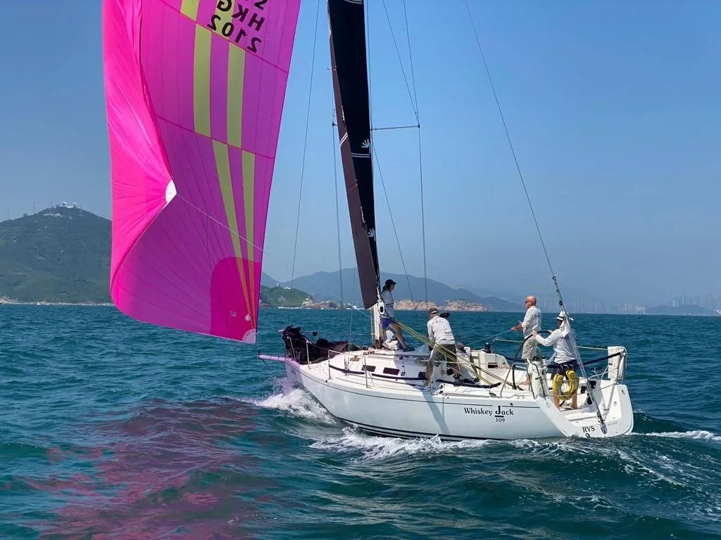 WHISKEY JACK reaching under a magenta and yellow asymmetric spinnaker with black mainsail, three crew in the cockpit