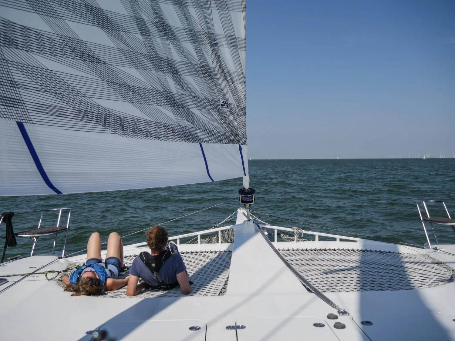 Grey X-Drive® genoa partially reefed on the catamaran, two young crew lying on the bow trampoline in the sun