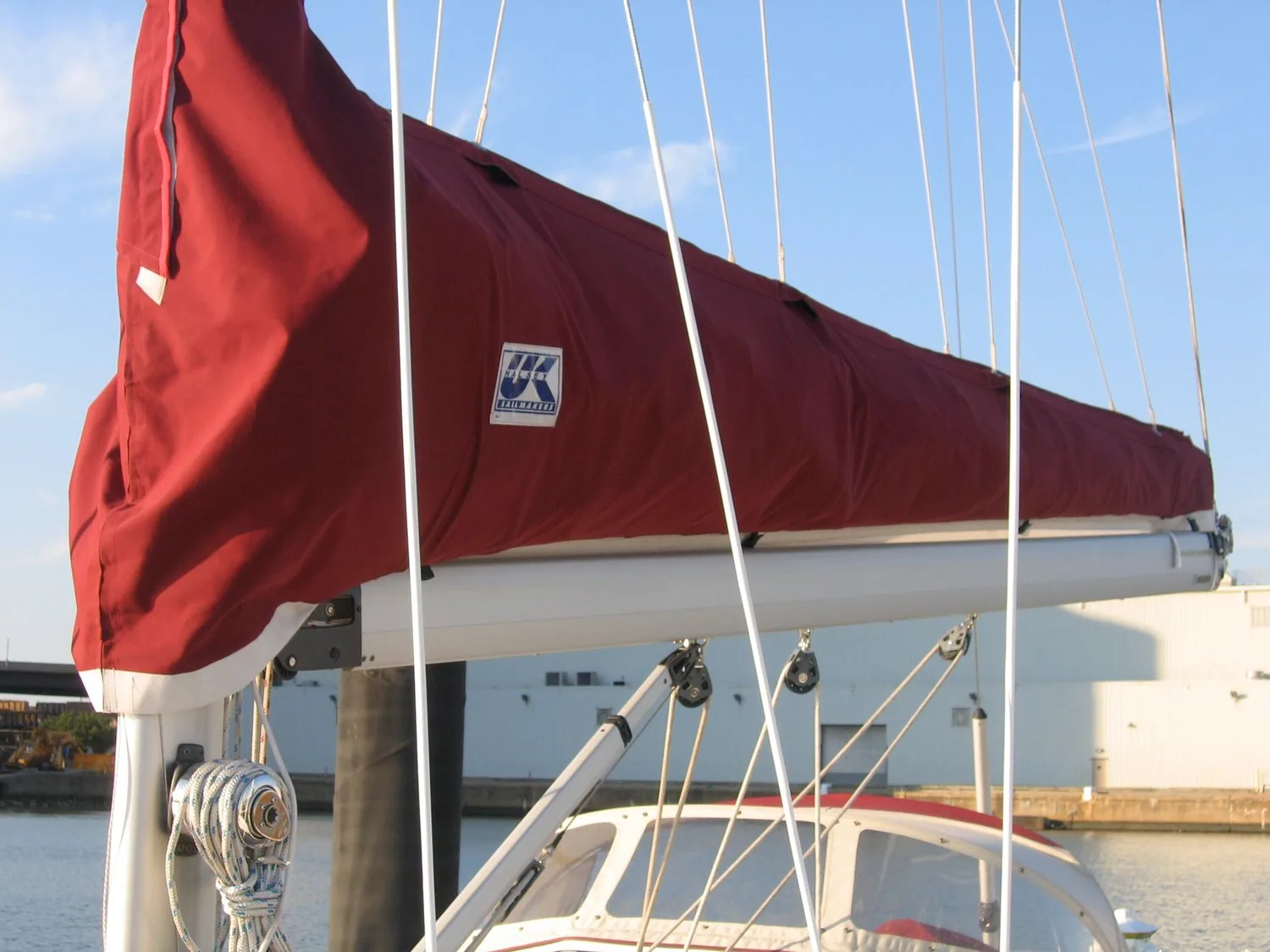 Red Lazy Cradle mainsail cover with UK Sailmakers logo zipped over a boom at the dock, lazy jack lines above