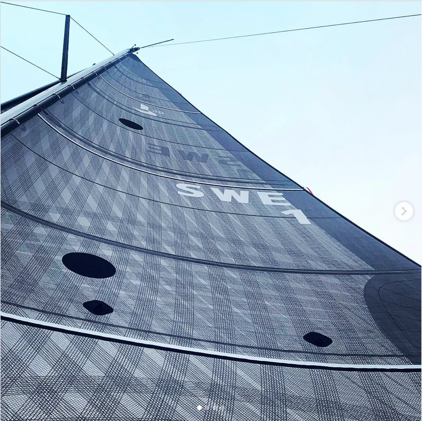 Looking up a grey X-Drive® mainsail marked SWE 1 from the deck, its panels curving against a pale sky