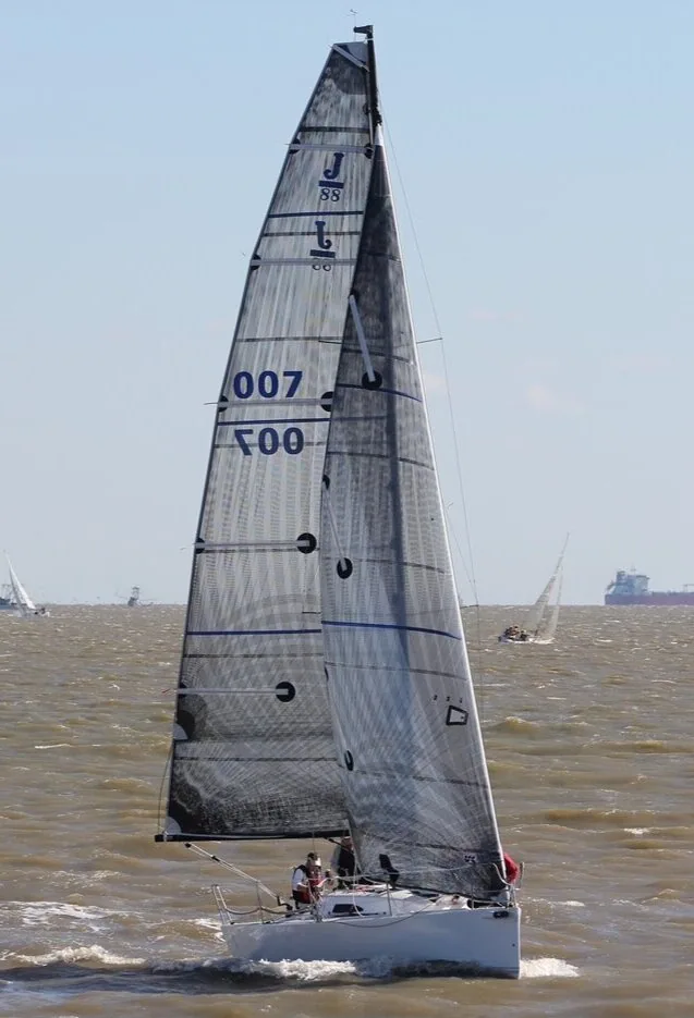 J/88 sail number 007 sailing upwind under grey carbon mainsail and jib on brown water, a freighter on the horizon