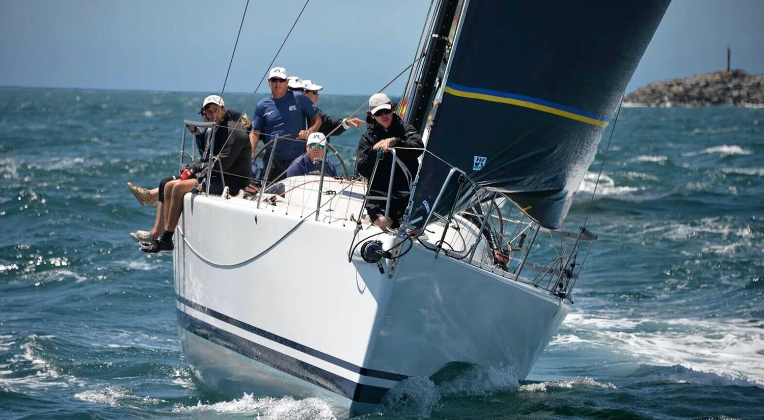 King 40 CHECKMATE bow-on under black sails with crew on the rail, Geoff Bishop at the wheel approaching the start