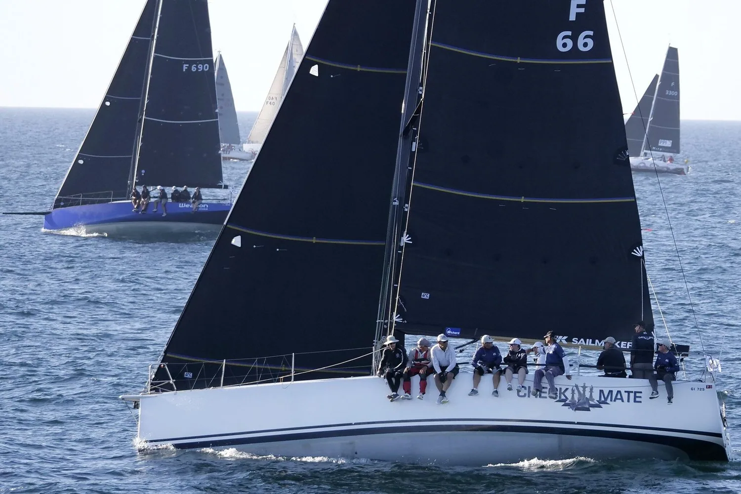 King 40 CHECKMATE (F 66) under black sails with crew on the rail at a race start, blue-hulled F 690 close behind