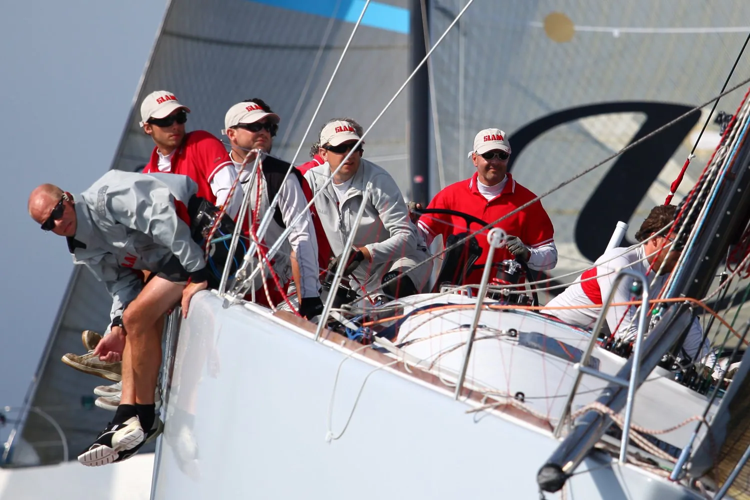 Race crew in red jackets hiking on the rail while the helmsman drives, UK Sailmakers logo on the sail behind