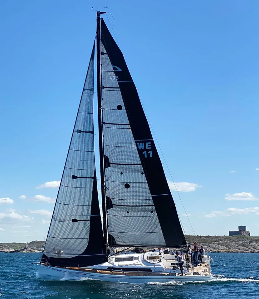 Sloop SWE 11 sailing upwind under a black mainsail and grey laminate genoa off a rocky shore with a stone tower