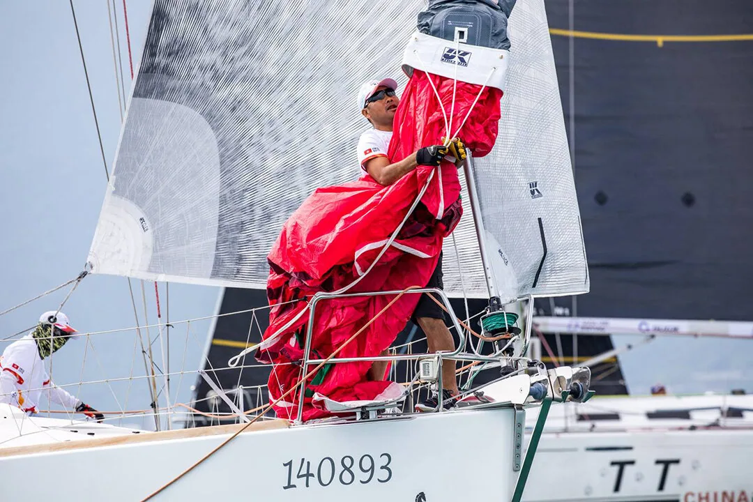 Bowman gathering a red spinnaker into its dousing sock on the foredeck of hull 140893 during a crowded regatta