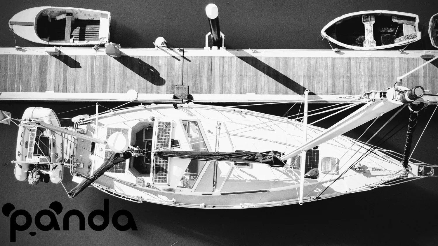 Black-and-white drone view straight down on Panda at a pontoon, showing her stern dinghy davits and deck solar panels