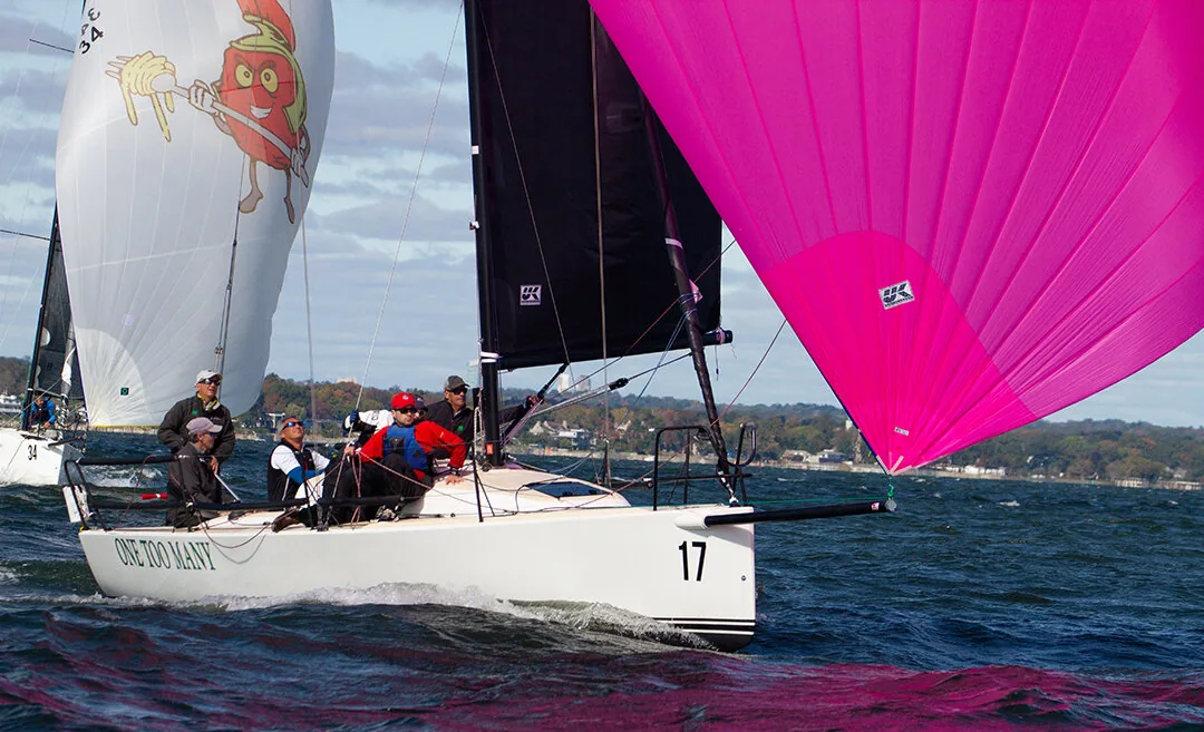 One Too Many, sail 17, powering downwind under a magenta asymmetric spinnaker with the UK logo, a rival's cartoon kite behind
