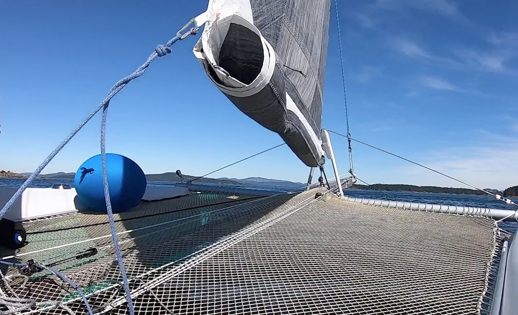 Reefed section of a grey headsail rolled and zipped away along the foot above a trampoline net
