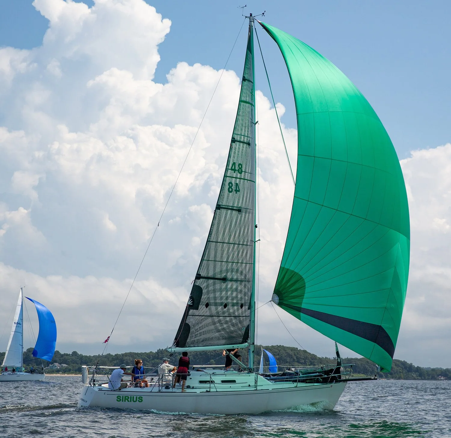 Sirius flying a green asymmetric spinnaker beside her black laminate mainsail, sail number 48, another boat astern