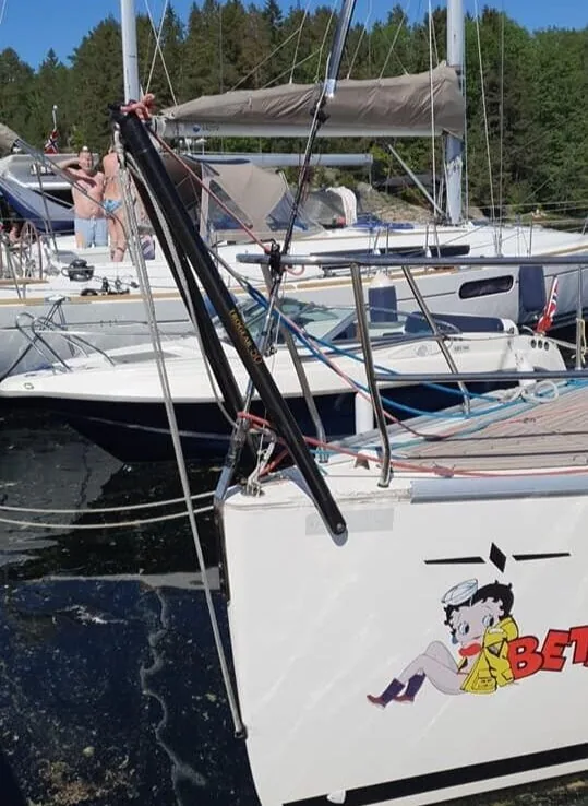 Black carbon bowsprit fitted to the bow of a small keelboat with a Betty Boop graphic on the hull, at a marina