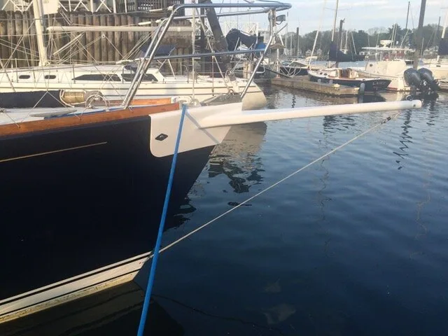 White bowsprit pole with a bobstay fitted to the bow of a dark blue-hulled yacht in a marina