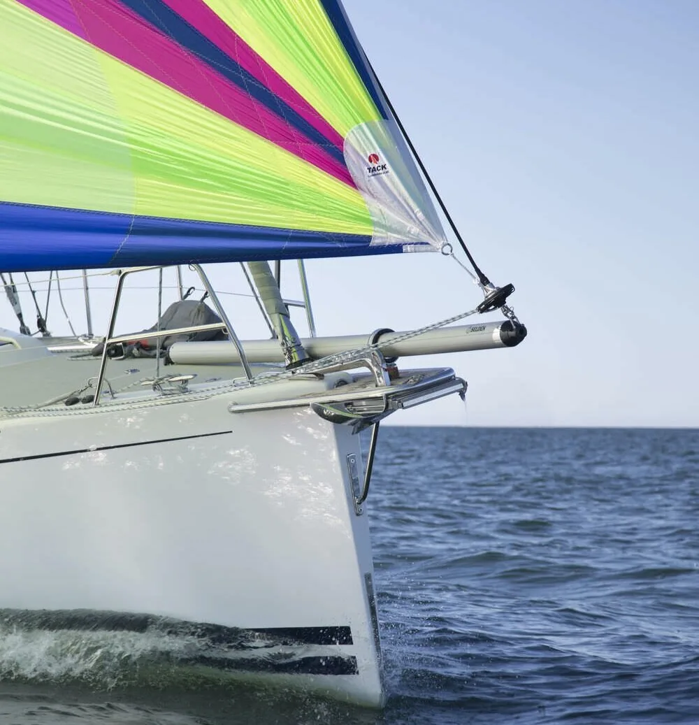 Retractable Seldén bowsprit on a white bow with a lime, magenta and blue asymmetric spinnaker tacked to its end