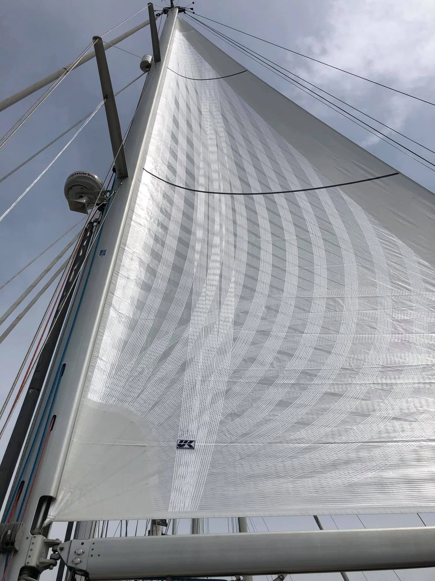Looking up a white mainsail from the boom, curved load-path tapes fanning across the panels, UK Sailmakers logo at the tack