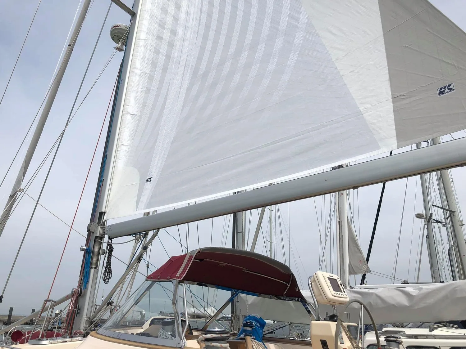 New white mainsail hoisted at the dock on a cruising yacht with a red bimini, UK Sailmakers logo near the clew