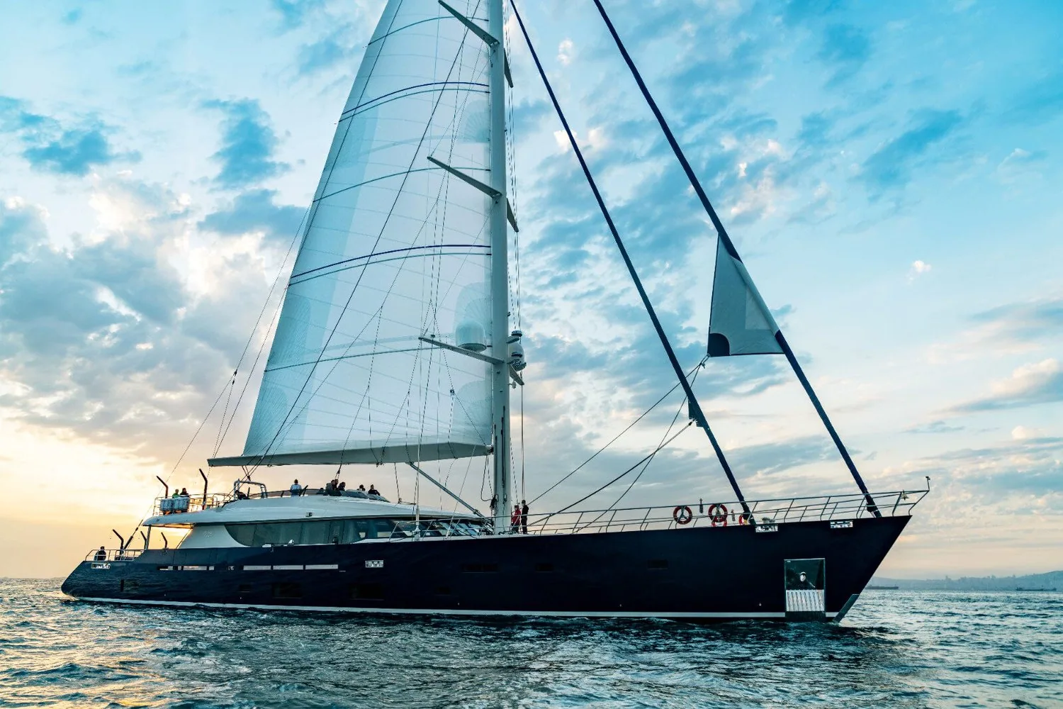 42-metre sailing superyacht with a dark navy hull under full white mainsail and headsail at sunset