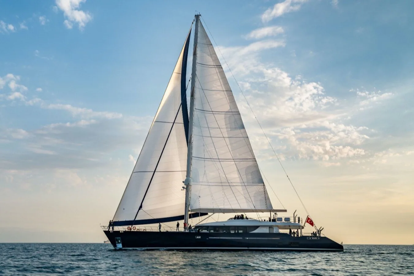 Profile of the 42-metre superyacht under mainsail and genoa, dark hull low in the water beneath scattered clouds