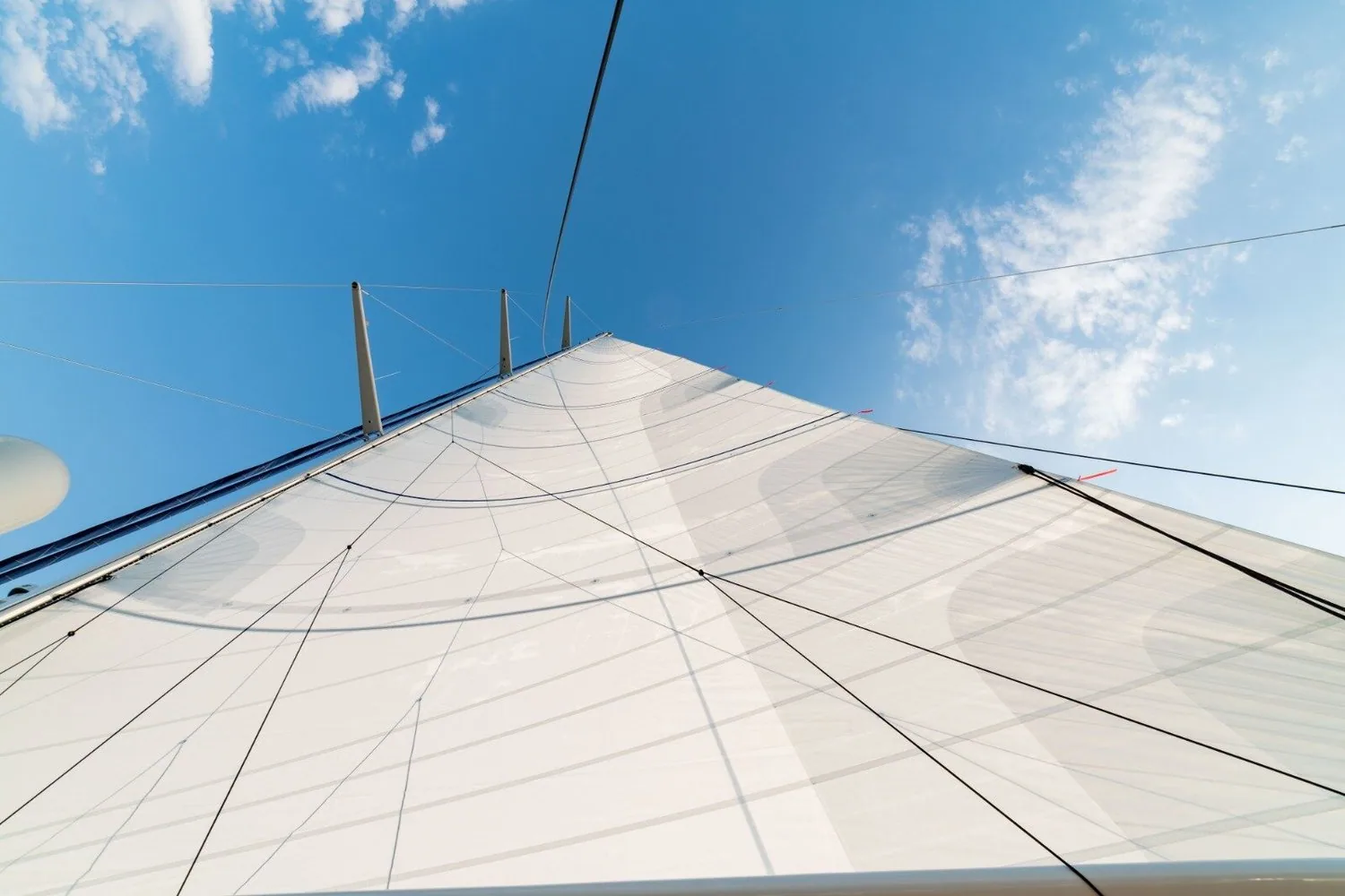 Looking up the towering white mainsail of the 42-metre superyacht against a blue sky with wispy clouds