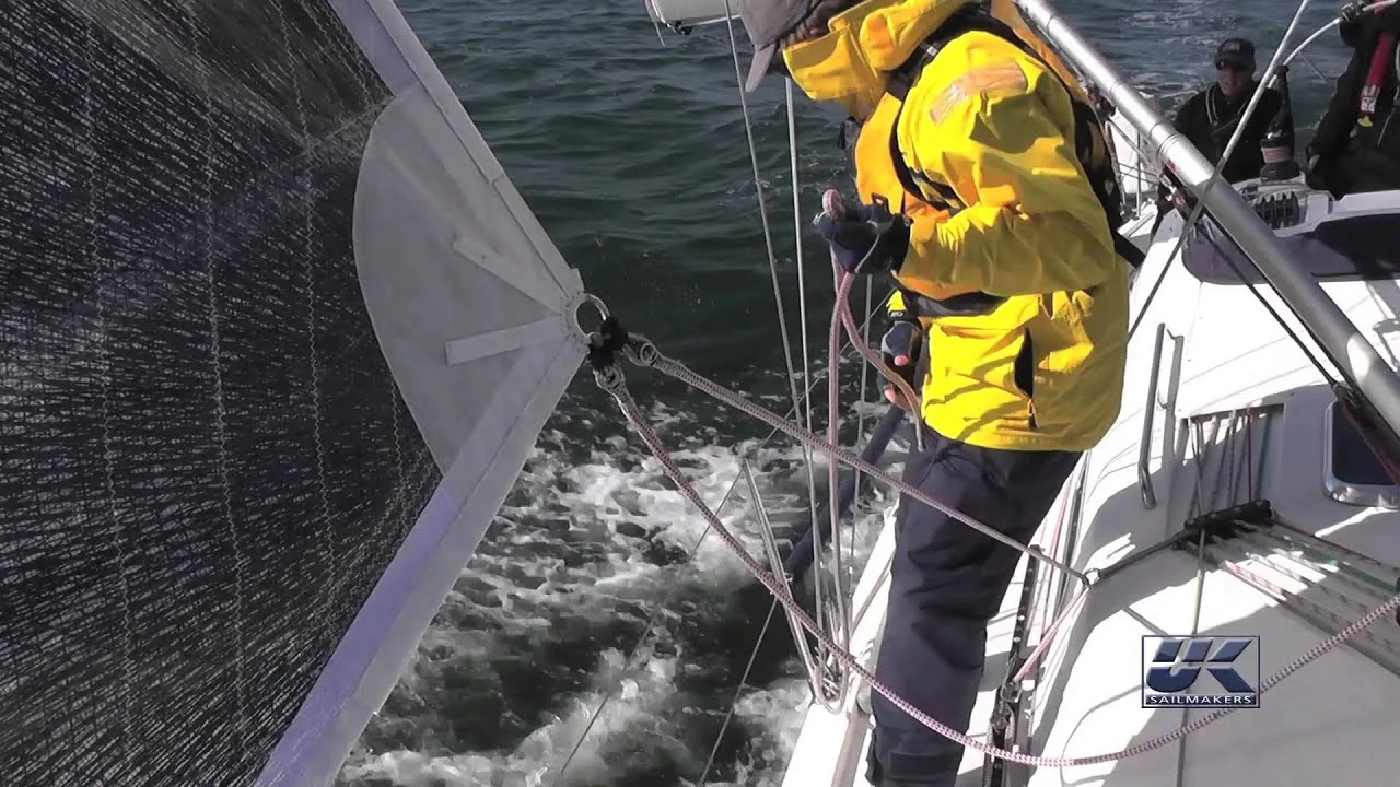 Video frame: a sailor in a yellow jacket on the side deck rigging an outboard sheet lead on the genoa clew
